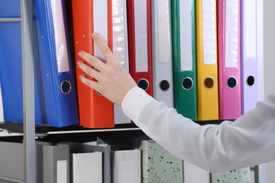 Photo of Woman taking folder with documents from shelf in office, closeup