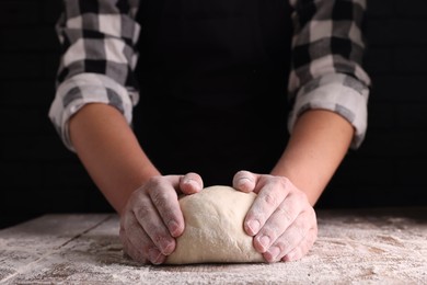 Photo of Man kneading dough at wooden table on dark background, closeup