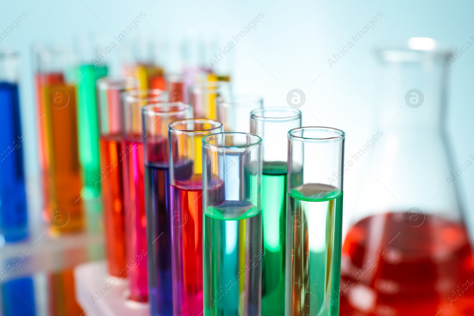 Photo of Different laboratory glassware with colorful liquids on turquoise background, closeup