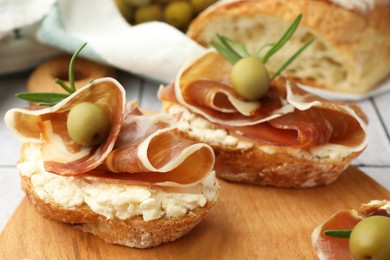 Photo of Tasty sandwiches with cured ham, rosemary and olives on wooden board, closeup