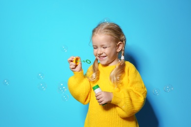 Cute little girl blowing soap bubbles on color background