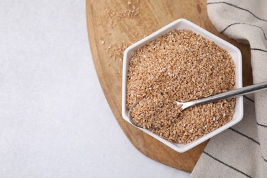 Photo of Dry wheat groats and spoon in bowl on light table, top view. Space for text