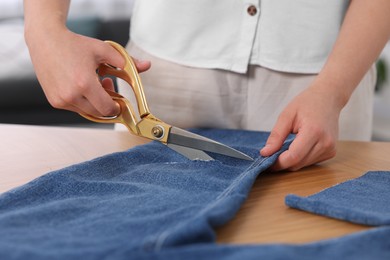 Photo of Woman making ripped jeans at wooden table, closeup