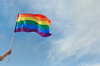 Gay man holding rainbow LGBT flag against blue sky. Space for text