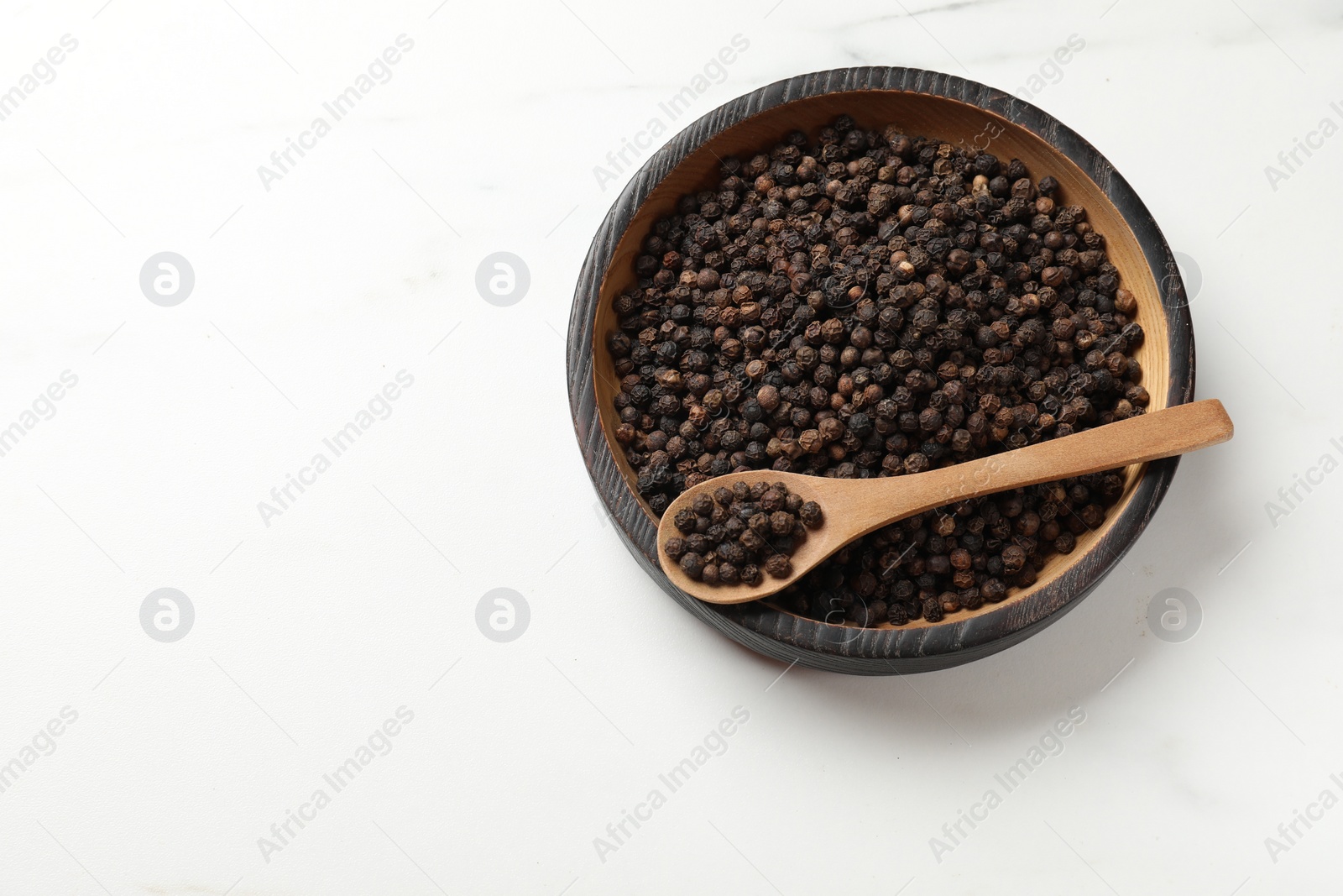 Photo of Aromatic spice. Black pepper in bowl and spoon on white table, top view. Space for text