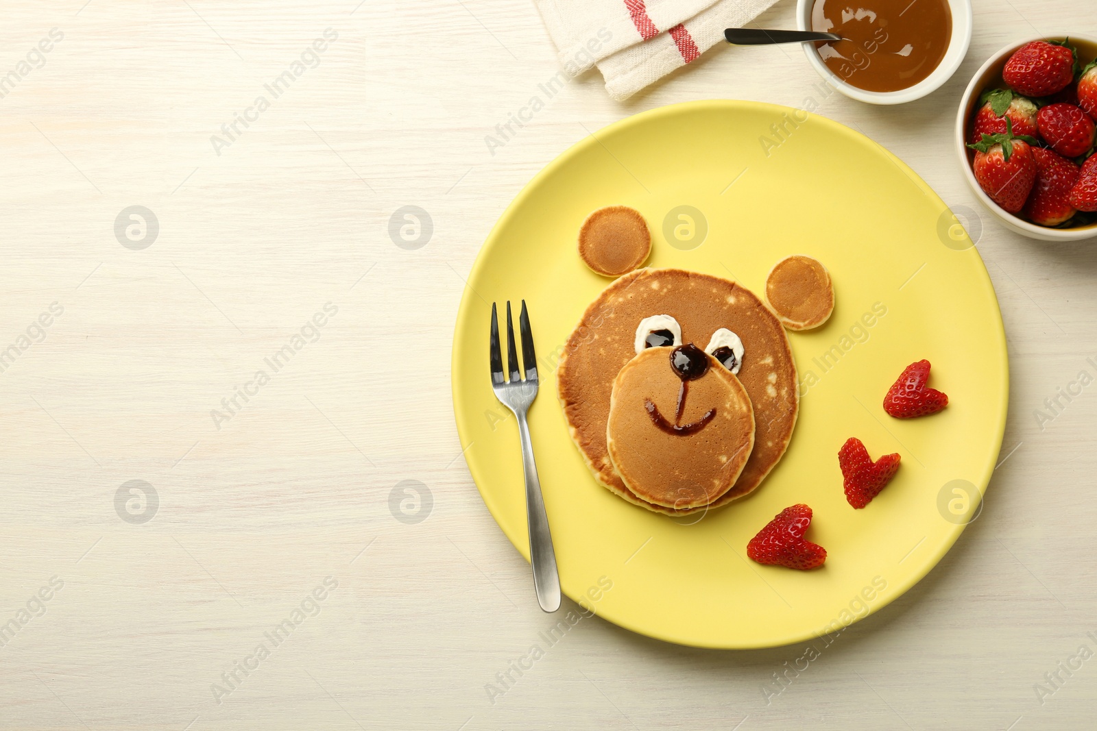 Photo of Creative serving for kids. Plate with strawberries, cute bear made of pancakes on light wooden table, flat lay. Space for text