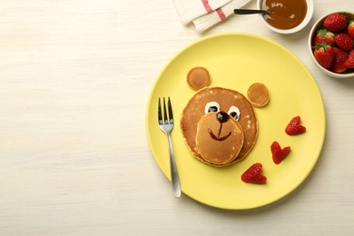 Creative serving for kids. Plate with strawberries, cute bear made of pancakes on light wooden table, flat lay. Space for text