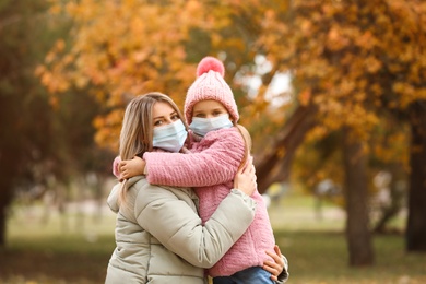 Mother and daughter in medical masks outdoors on autumn day. Protective measures during coronavirus quarantine
