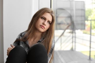 Depressed young woman sitting near window