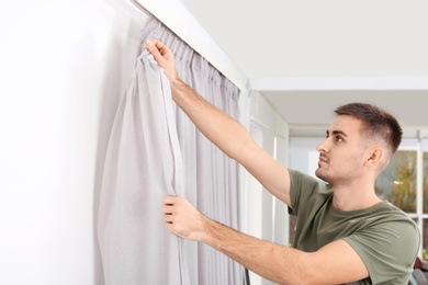 Photo of Man hanging window curtain indoors. Interior decor element