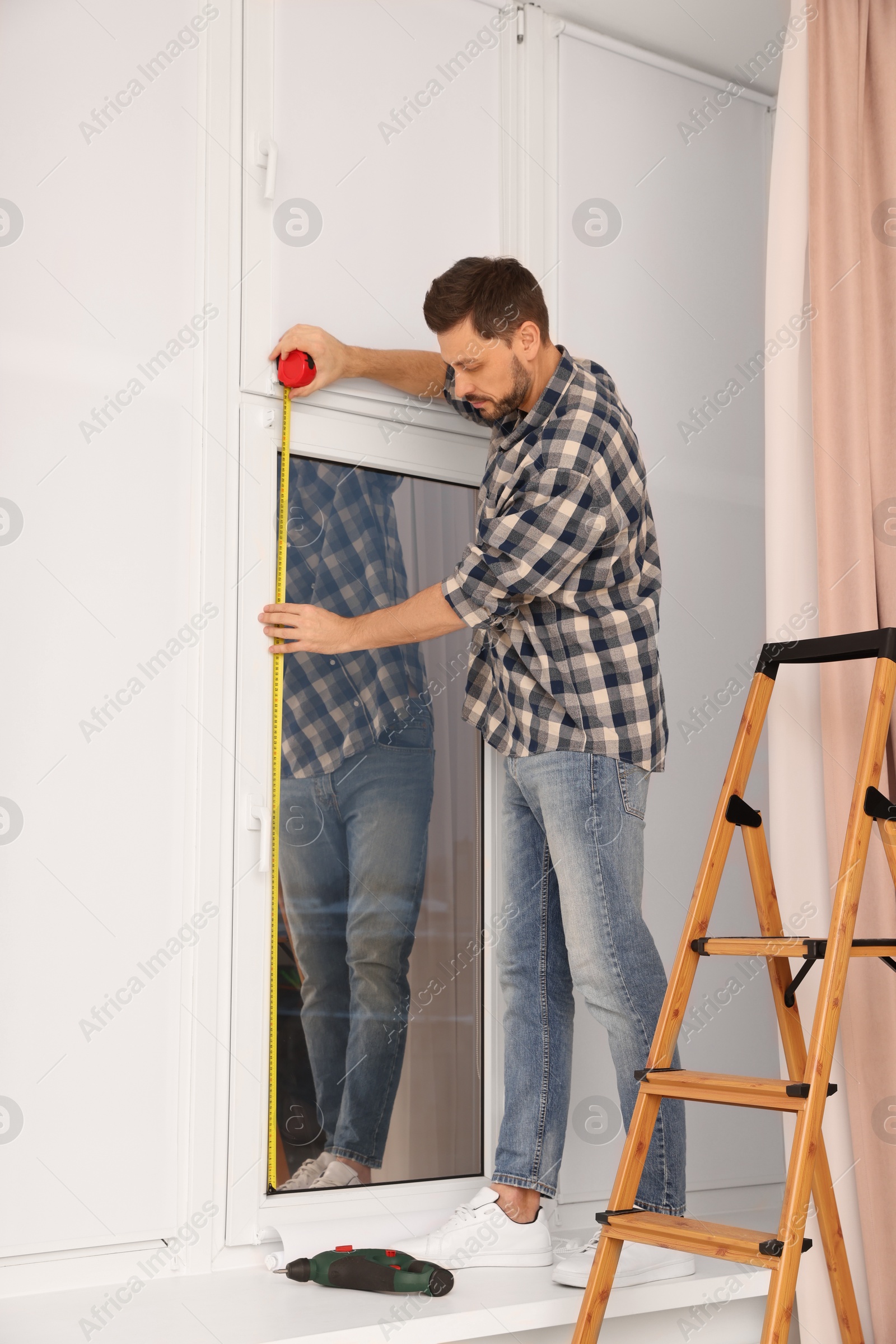 Photo of Man measuring window with tape indoors. Roller blinds installation