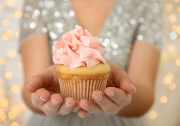 Woman holding tasty cupcake for Valentine's Day against blurred lights, closeup