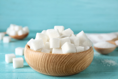 Photo of Refined sugar cubes in bowl on blue wooden table