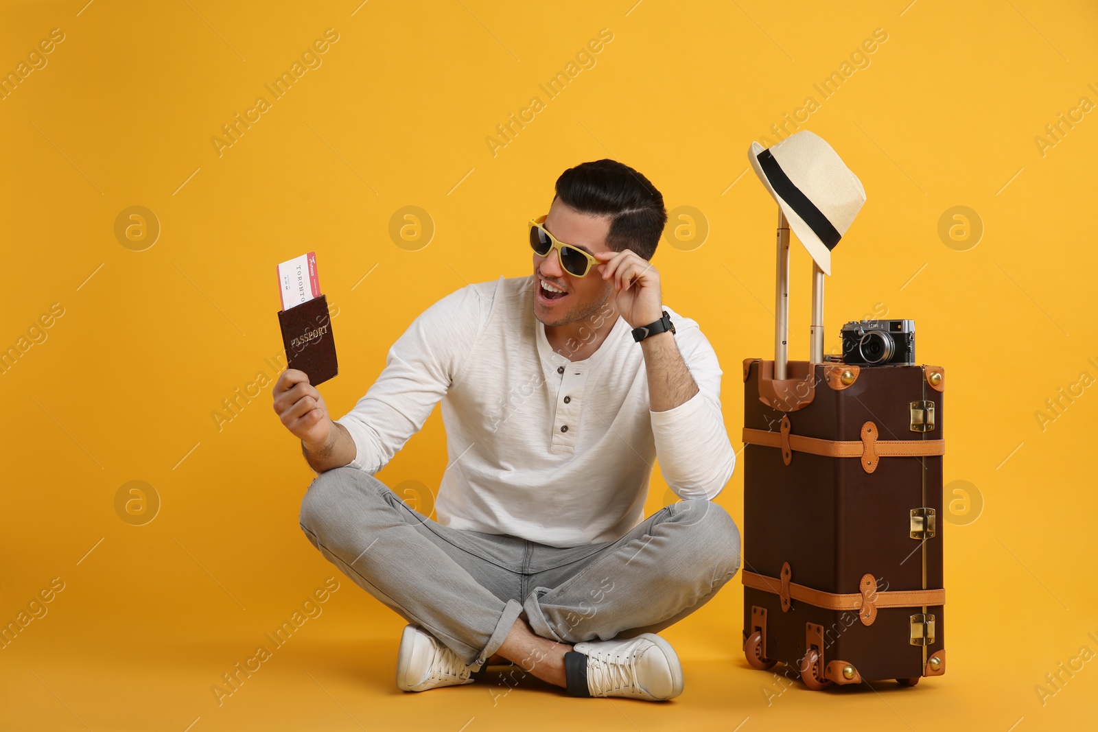 Photo of Excited male tourist holding passport with ticket near suitcase on yellow background