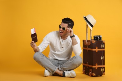 Photo of Excited male tourist holding passport with ticket near suitcase on yellow background