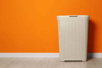 Empty laundry basket near orange wall indoors, space for text