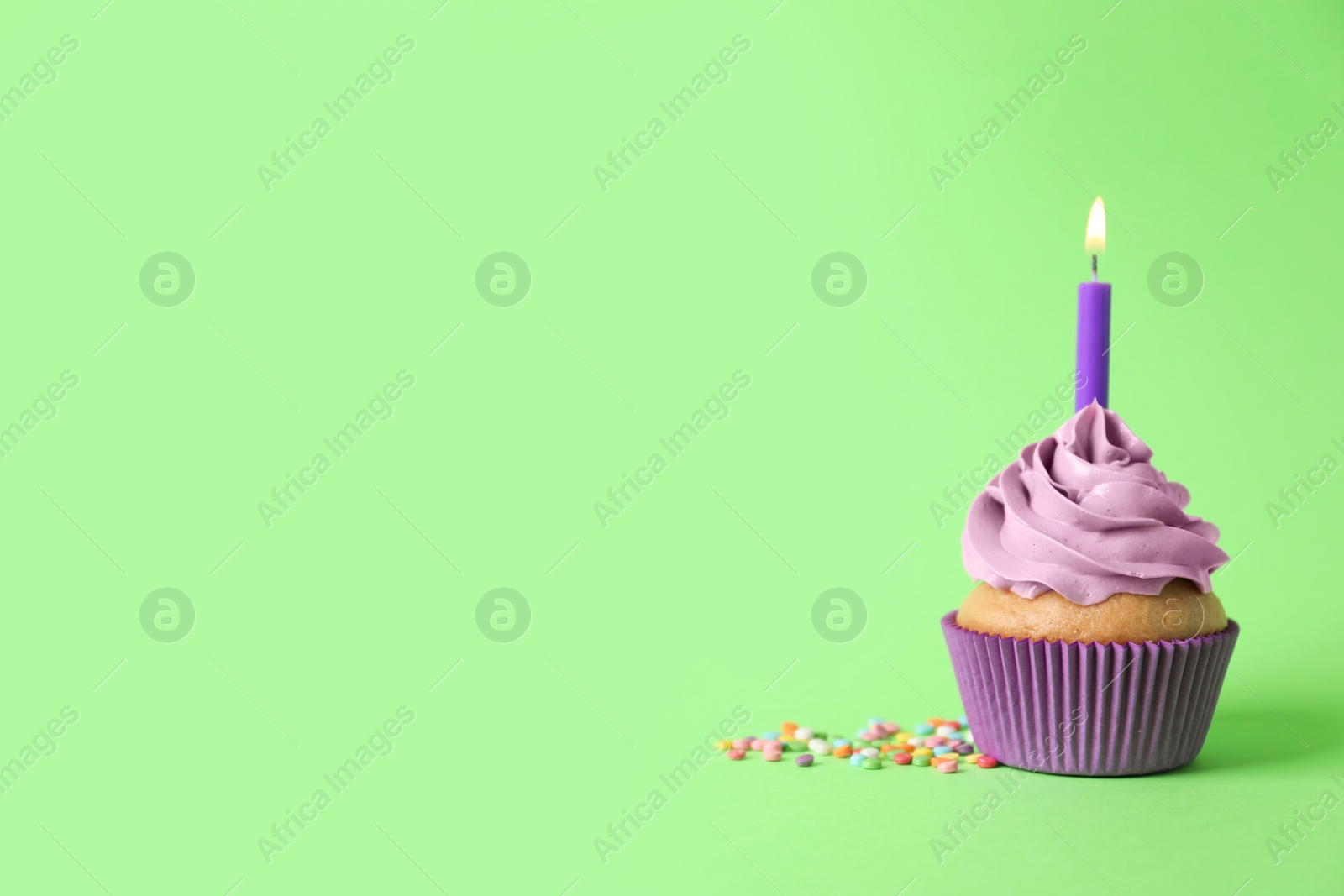 Photo of Delicious birthday cupcake with burning candle and sprinkles on green background, space for text