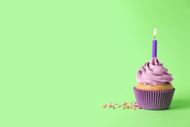 Delicious birthday cupcake with burning candle and sprinkles on green background, space for text