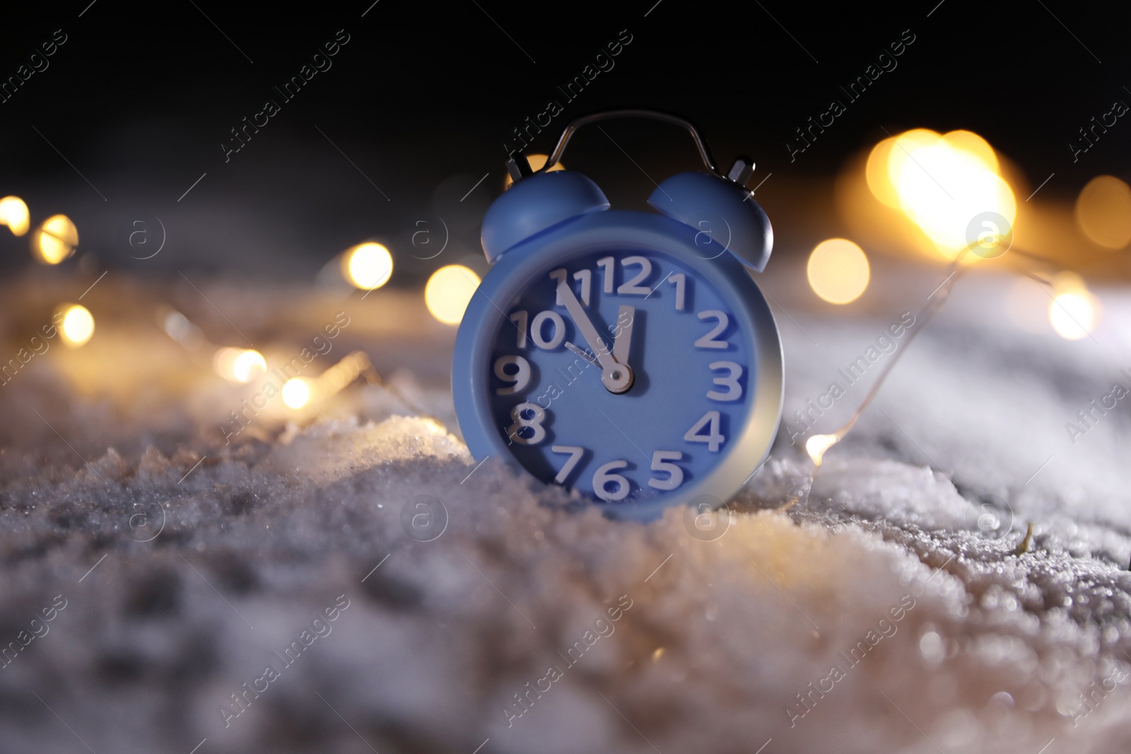 Photo of Alarm clock and Christmas lights on white snow outdoors. Midnight countdown