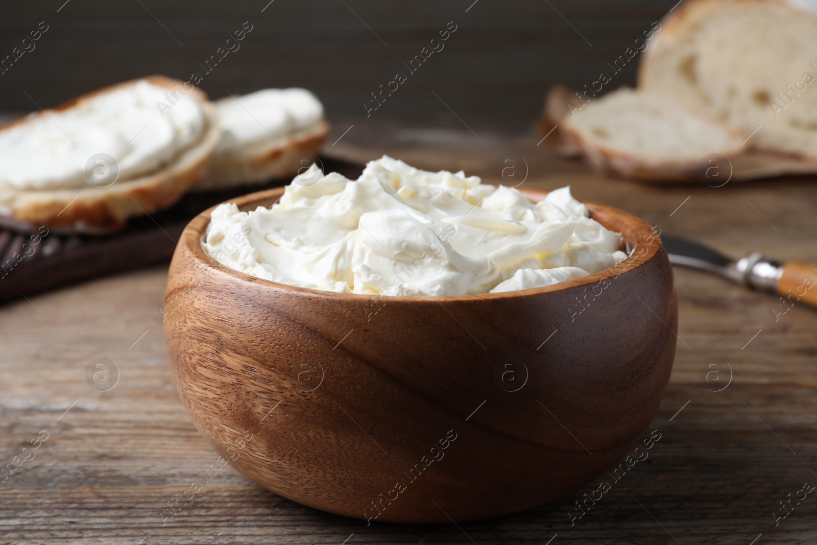 Photo of Bowl of tasty cream cheese and fresh bread on wooden table