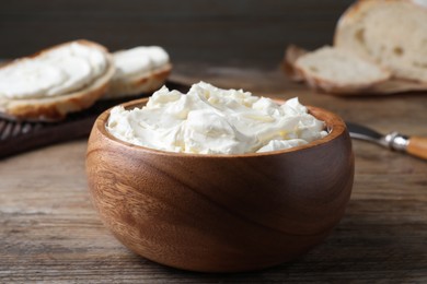 Bowl of tasty cream cheese and fresh bread on wooden table