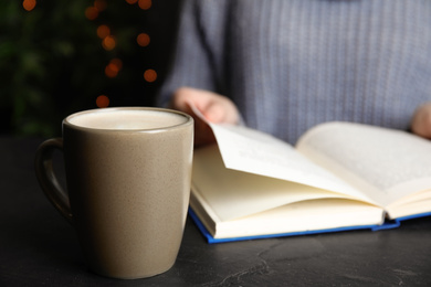 Woman with coffee reading book at table, focus on cup