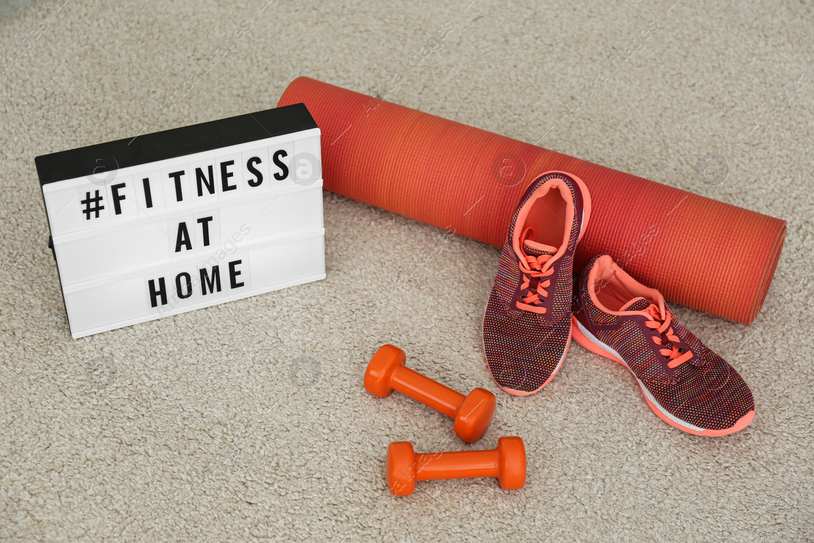 Photo of Sport equipment and lightbox with hashtag FITNESS AT HOME on carpet. Message to promote self-isolation during COVID‑19 pandemic