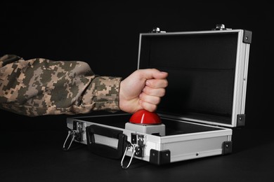 Photo of Serviceman pressing red button of nuclear weapon at black table, closeup. War concept