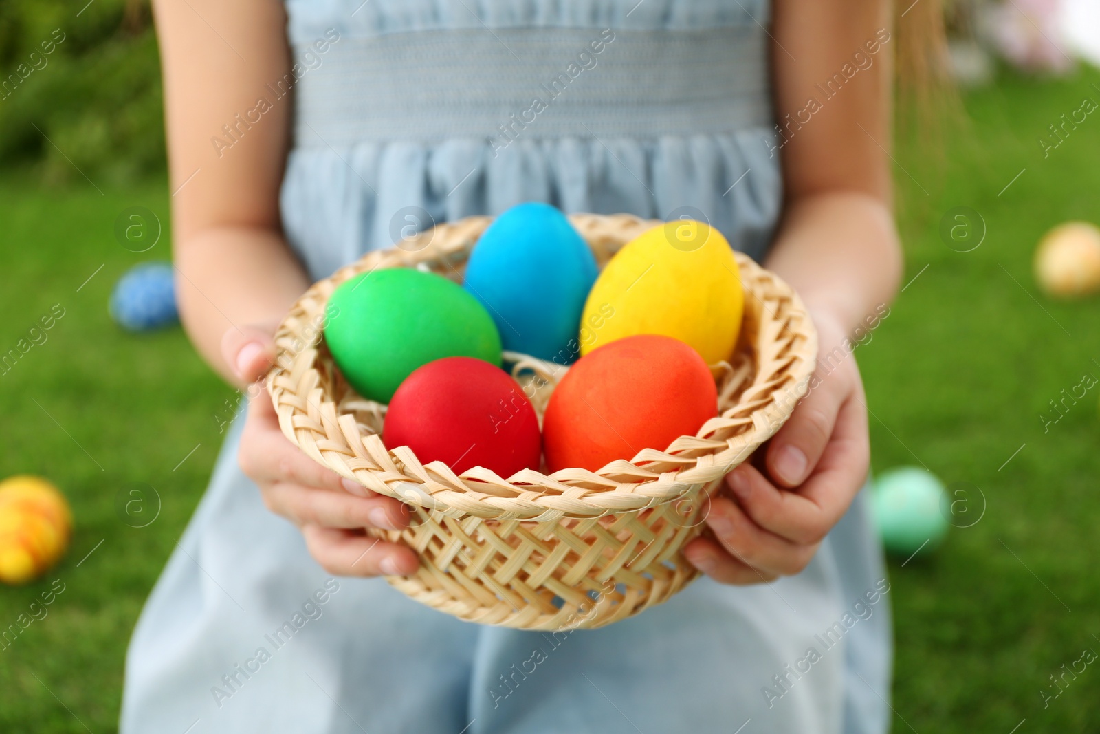 Photo of Cute little girl with basket full of Easter eggs outdoors, closeup