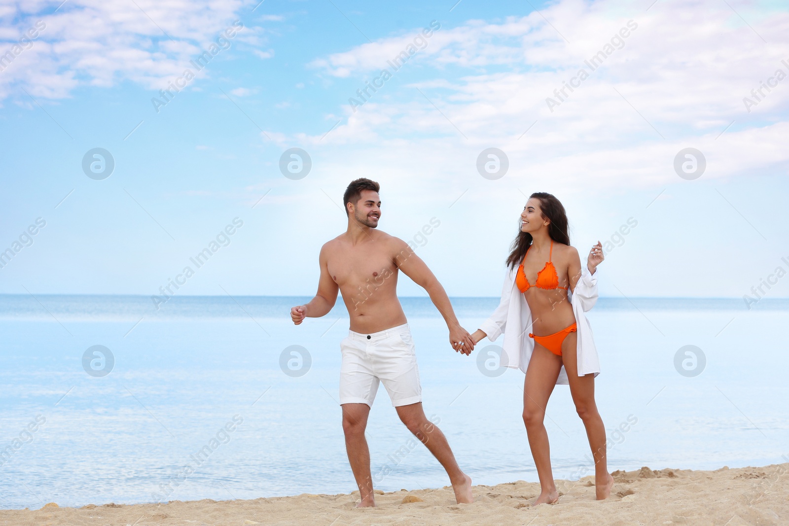 Photo of Happy young couple walking together on beach near sea