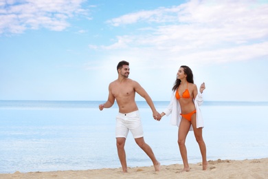 Happy young couple walking together on beach near sea