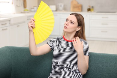 Photo of Woman waving yellow hand fan to cool herself on sofa at home