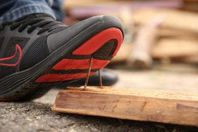 Photo of Careless worker stepping on nails in wooden plank outdoors, closeup