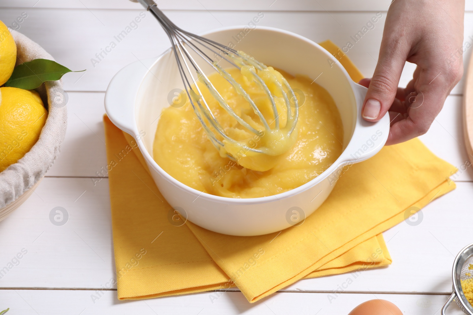 Photo of Woman cooking lemon curd at white wooden table, closeup