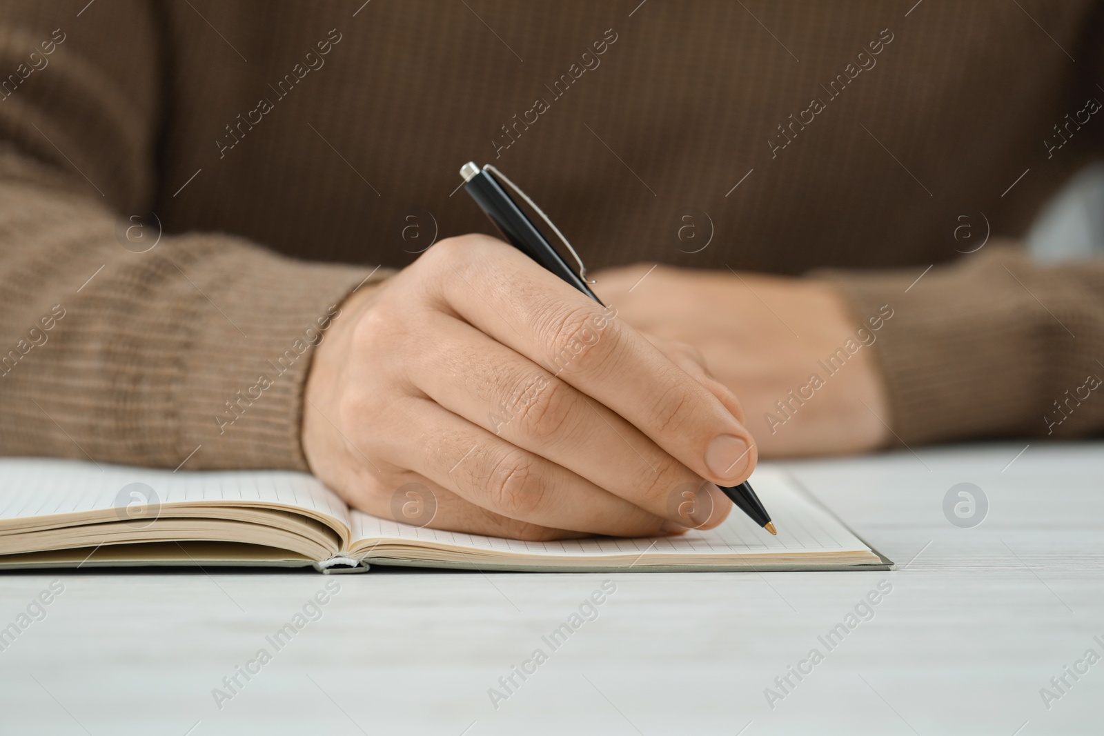 Photo of Man writing in notebook at white table, closeup