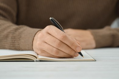 Man writing in notebook at white table, closeup