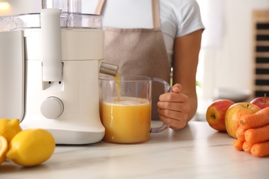 Photo of Young woman making tasty fresh juice at table in kitchen, closeup