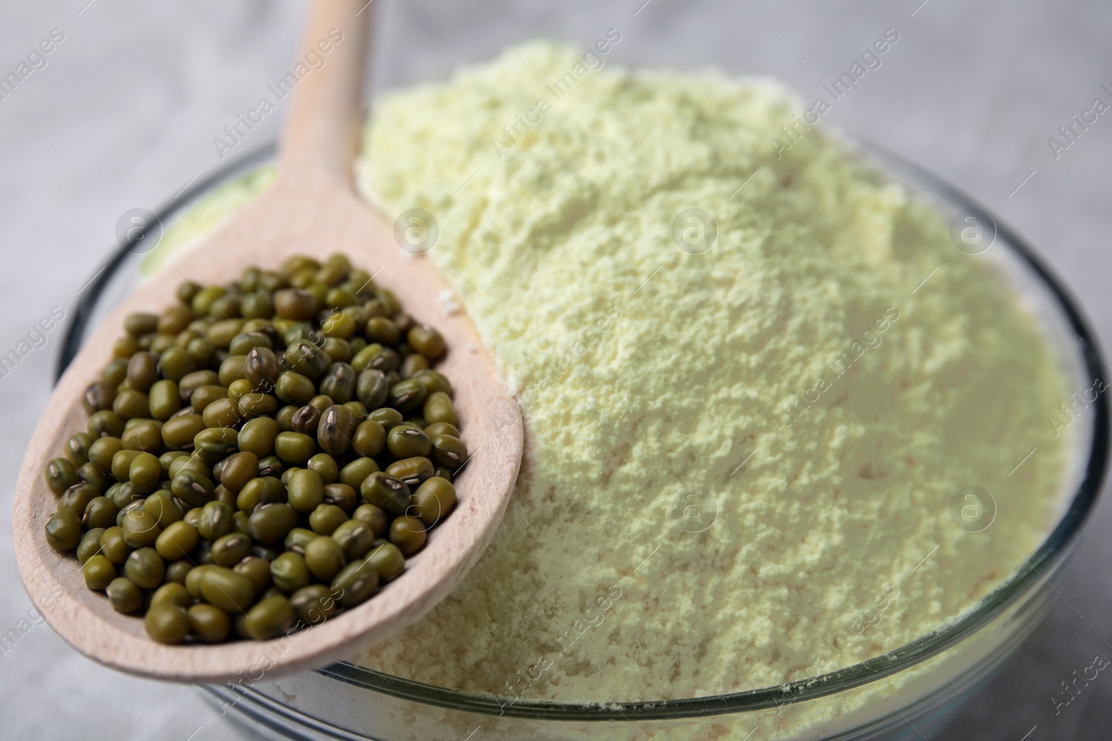 Photo of Bowl of flour, spoon and mung beans on light grey cloth, closeup