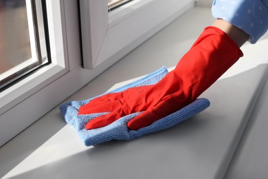 Photo of Woman cleaning window sill with rag at home, closeup