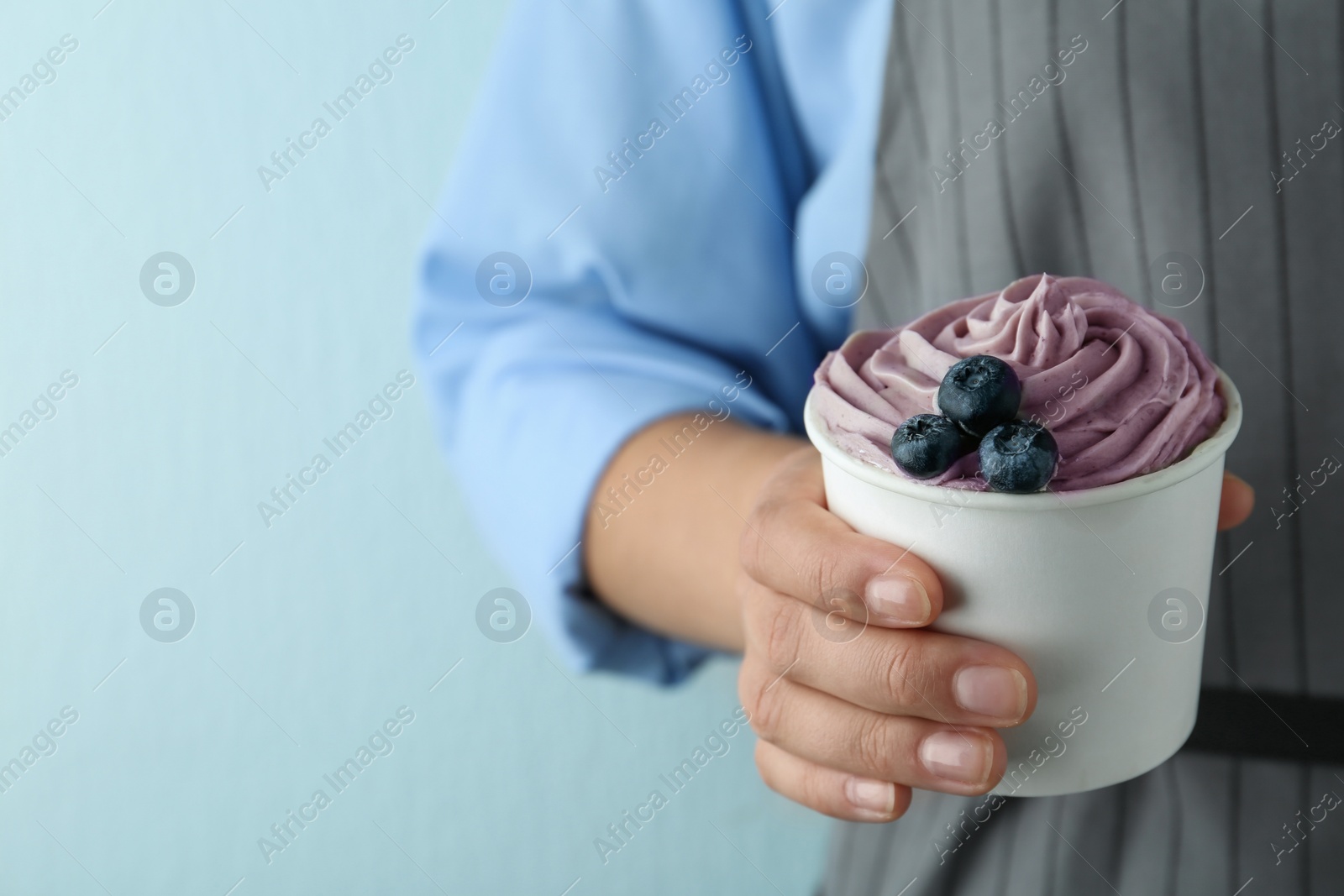 Photo of Woman holding cup with tasty frozen yogurt on blue background, closeup