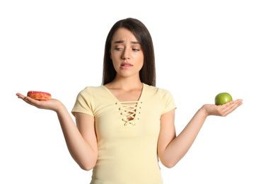 Photo of Doubtful woman choosing between apple and doughnut on white background
