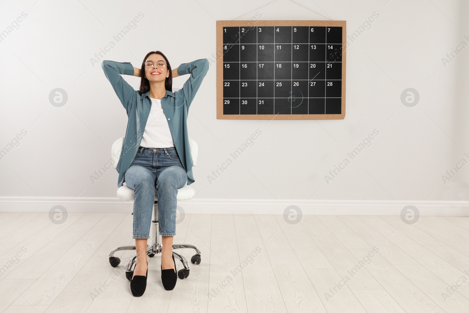 Photo of Beautiful young woman sitting near board calendar indoors