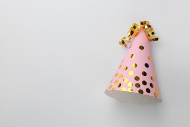 One pink party hat with serpentine streamers on light background, top view. Space for text