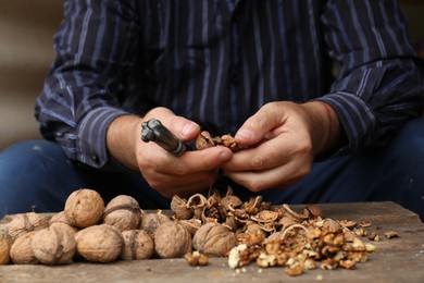 Photo of Man cracking walnuts at wooden table, closeup