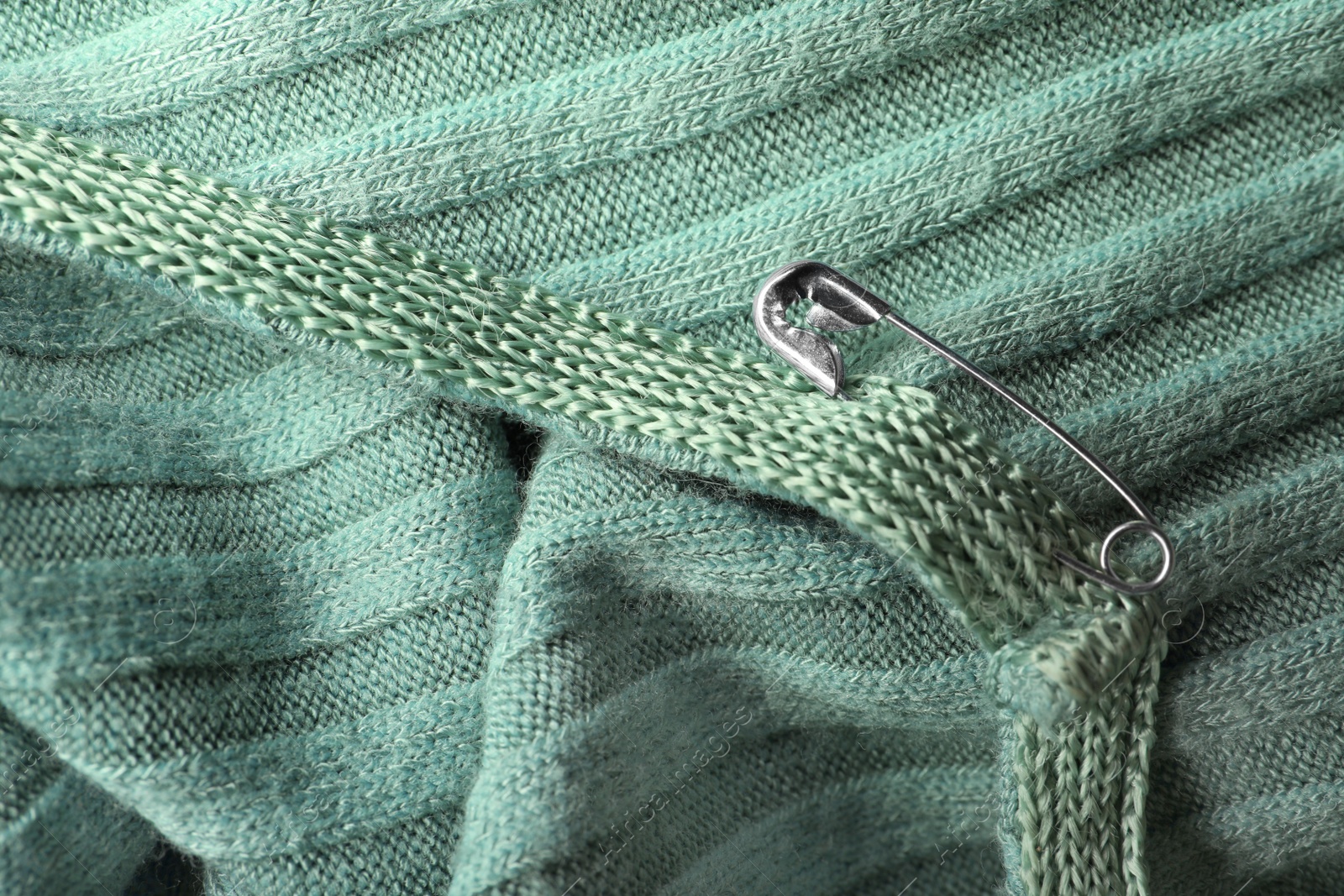 Photo of Metal safety pin on light green fabric, closeup