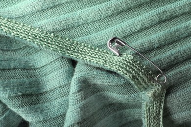 Metal safety pin on light green fabric, closeup