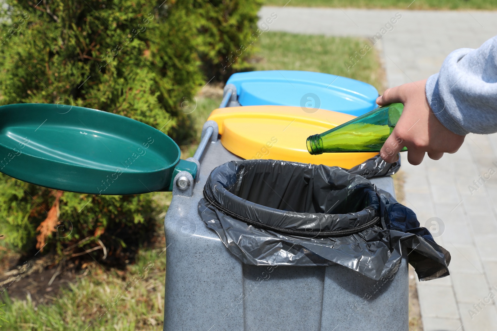 Photo of Woman throwing glass bottle in bin outdoors, closeup. Recycling concept