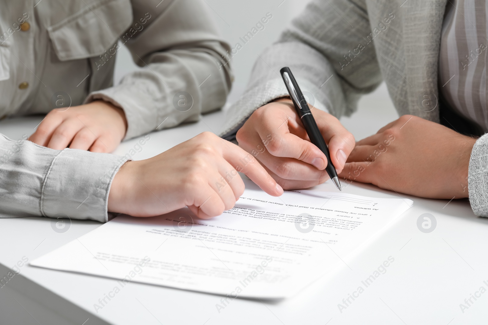 Photo of Woman pointing at document and man putting signature at white table, closeup