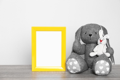 Photo of Photo frame and adorable toy bunnies on table against light background, space for text. Child room elements