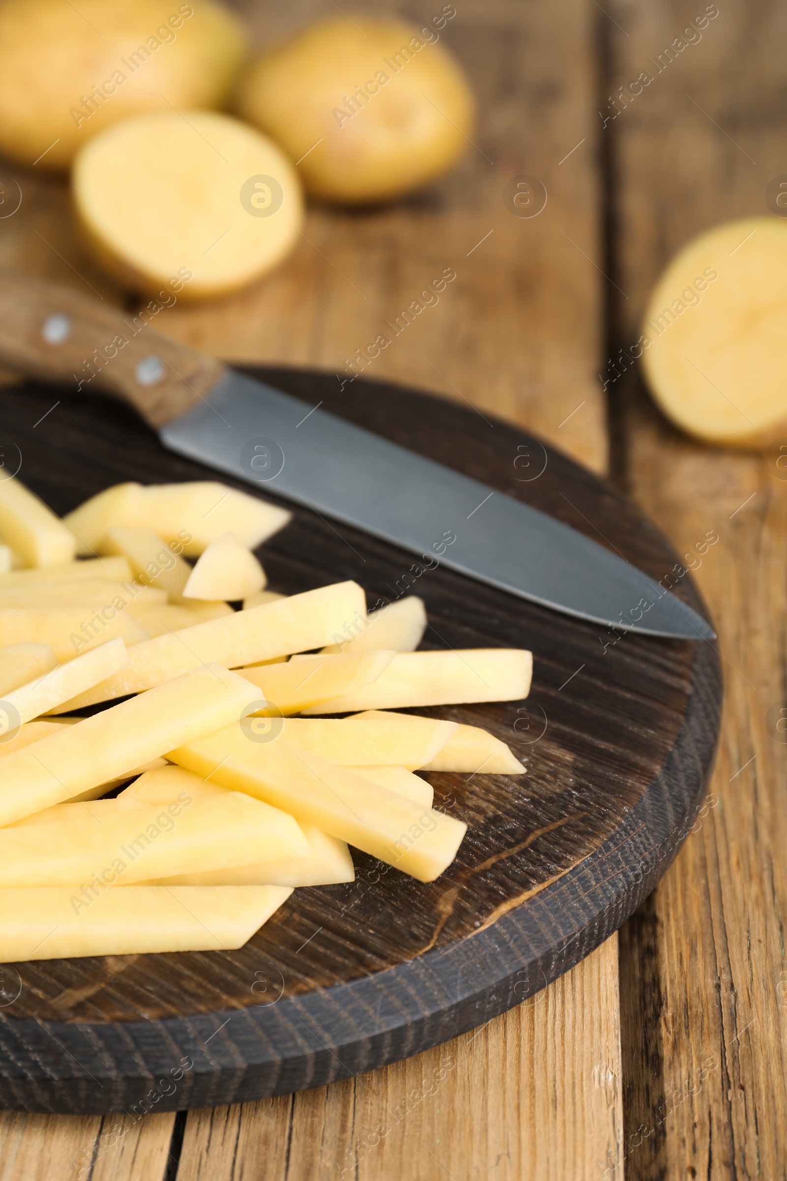 Photo of Cut potatoes and knife on wooden table, closeup. Cooking delicious french fries